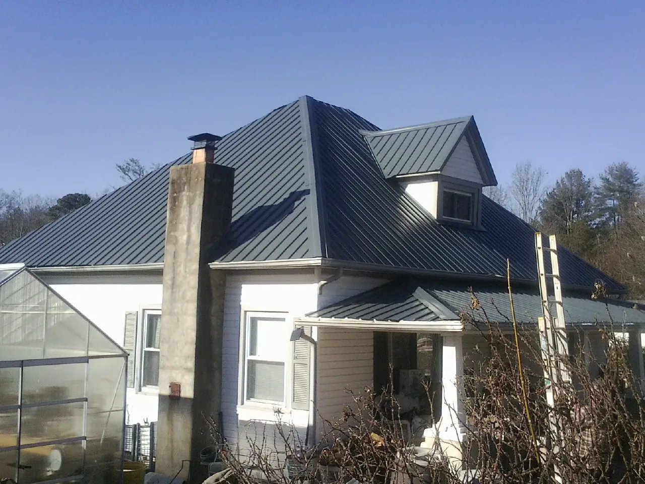 Dark blue standing seam metal roof on a white farmhouse with dormer — Slate & Tile Roof Repair by Roofing Brothers in Raphine
