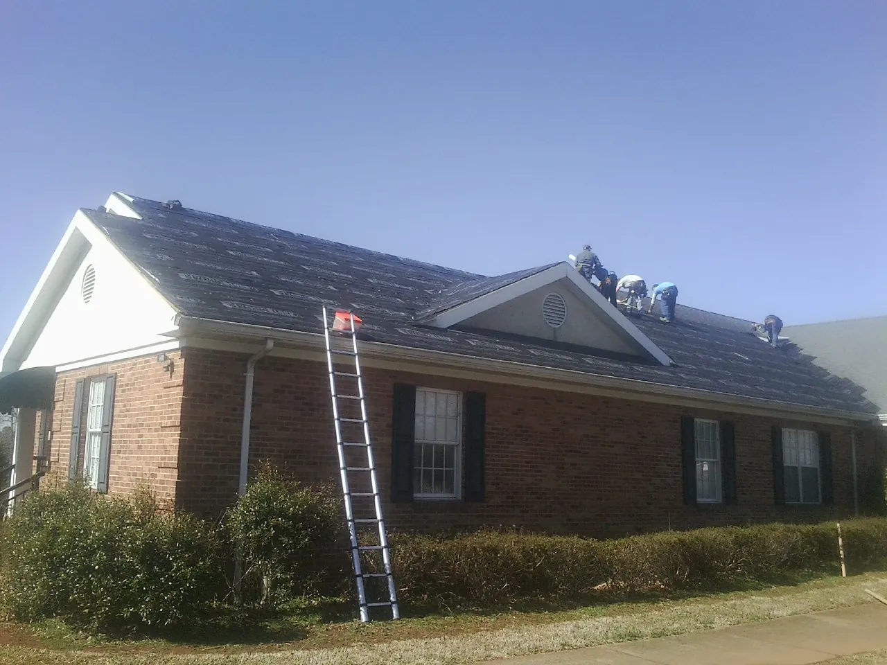 Crew tearing shingles off a brick ranch roof with a ladder set — Metal Roof Repair work by our crew in Raphine