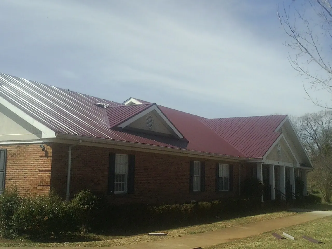 Red metal roof with gabled entries on a long brick building, from a Hail Damage Roof Repair job in Raphine