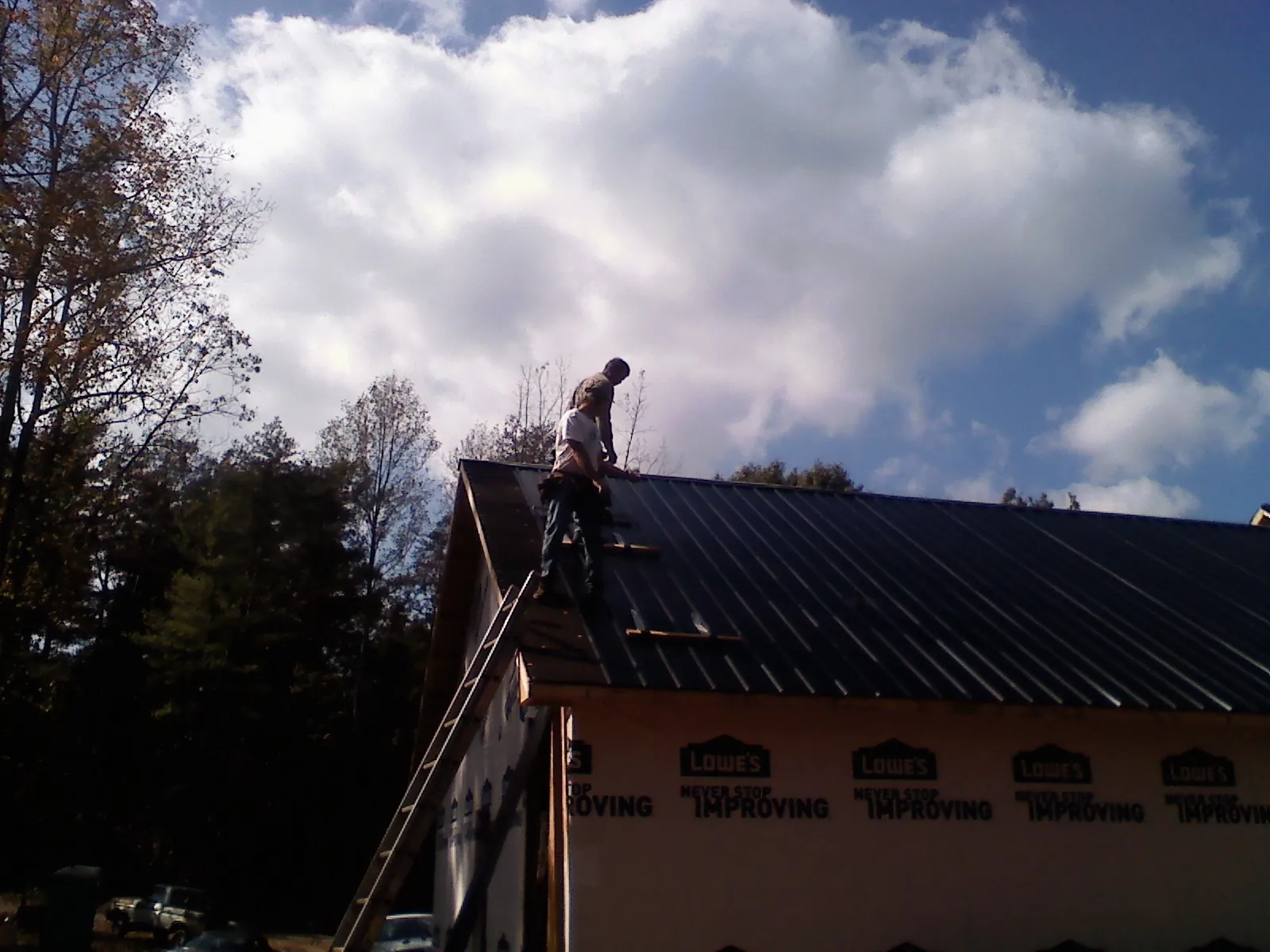 Roofer fastening dark metal panels high against a cloudy sky, from a Roof Inspection job in Raphine